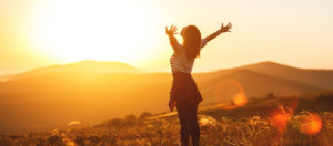 Happy woman jumping and enjoying life in field at sunset in mountains